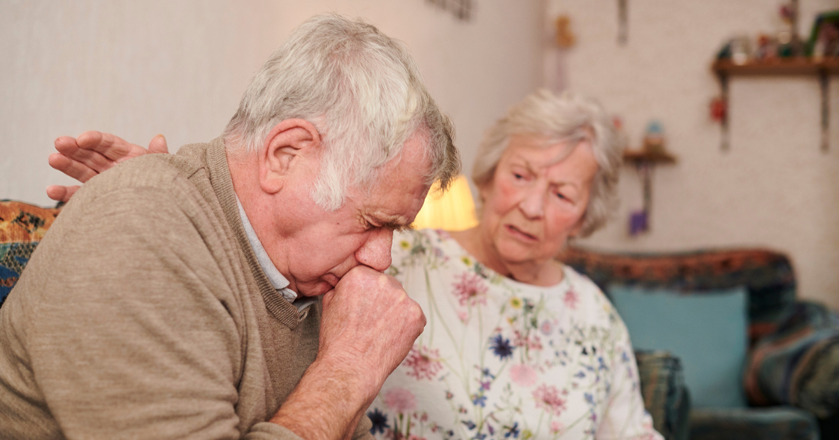 Older man coughing while wife pats his back