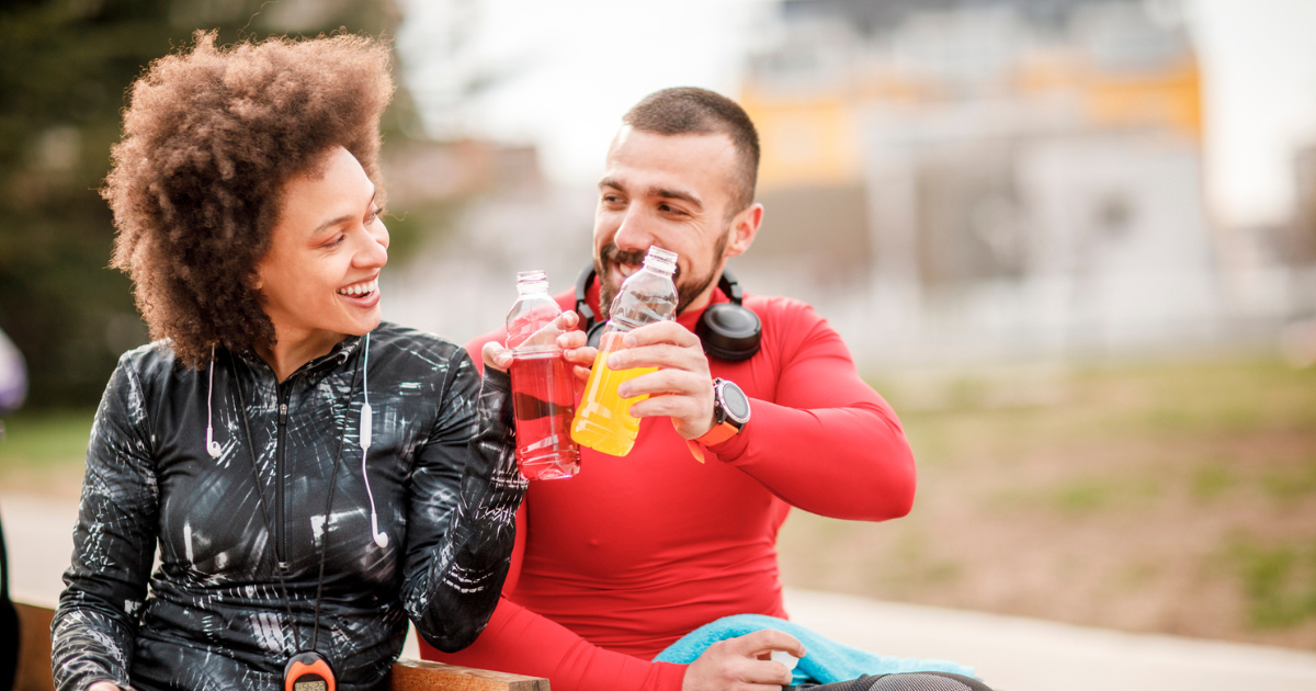 Man and woman sitting on bench drinking sports drinks
