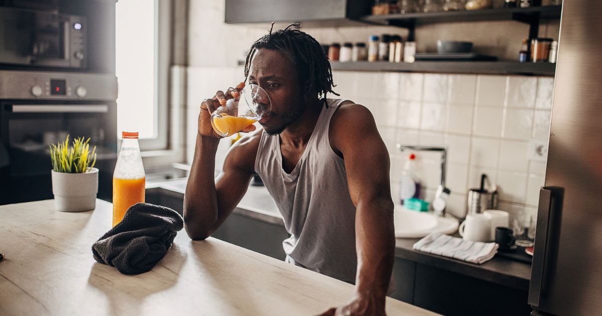 Man drinking a glass of orange juice in his kitchen