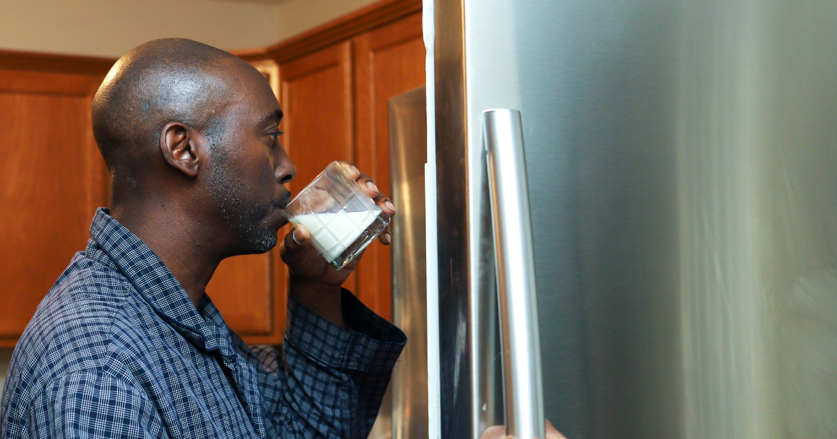 Man drinking a glass of milk in front of an open fridge