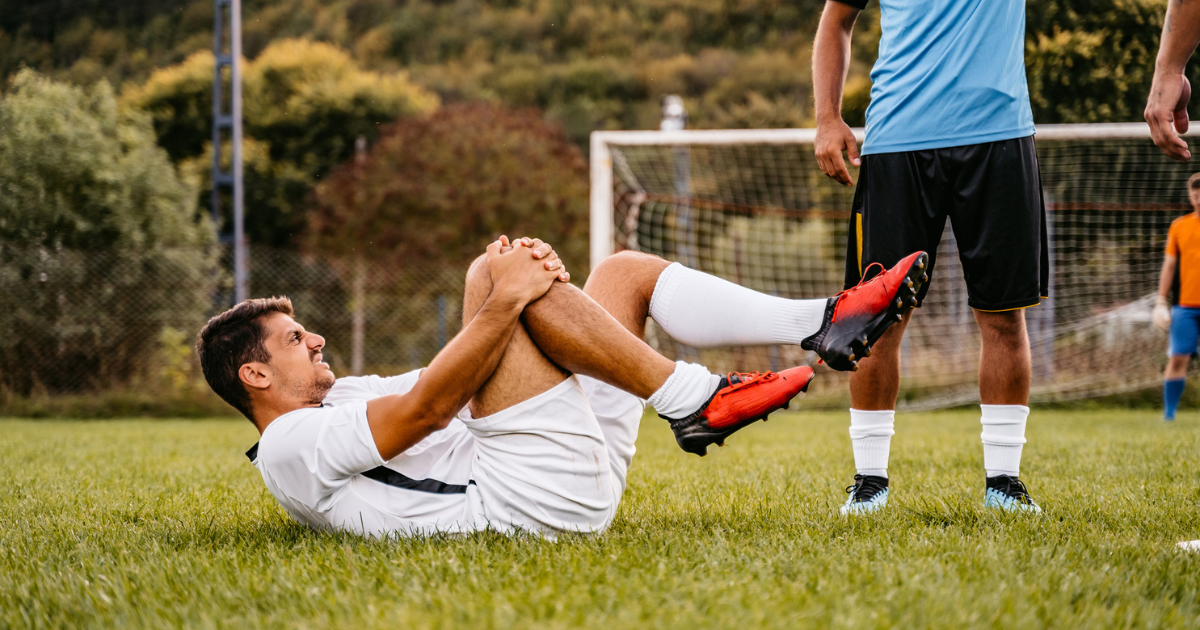 Soccer player holding his knee lying down on field