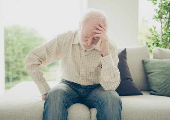 Older man sitting on the couch holding his head