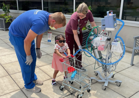 Genesis Sanchez-Vasquez pushes a tiny shopping cart with help from Chad Doerneman and Katie Stehlik.