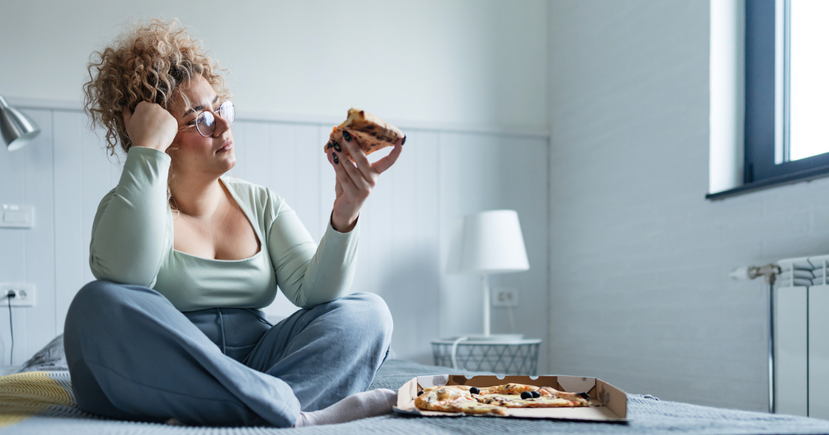 Woman eating pizza in bed