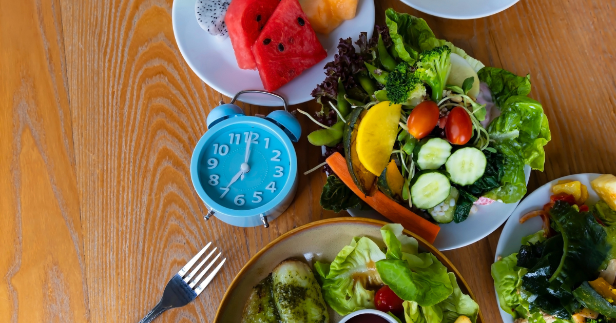 Alarm clock on table surrounded by plates of food.