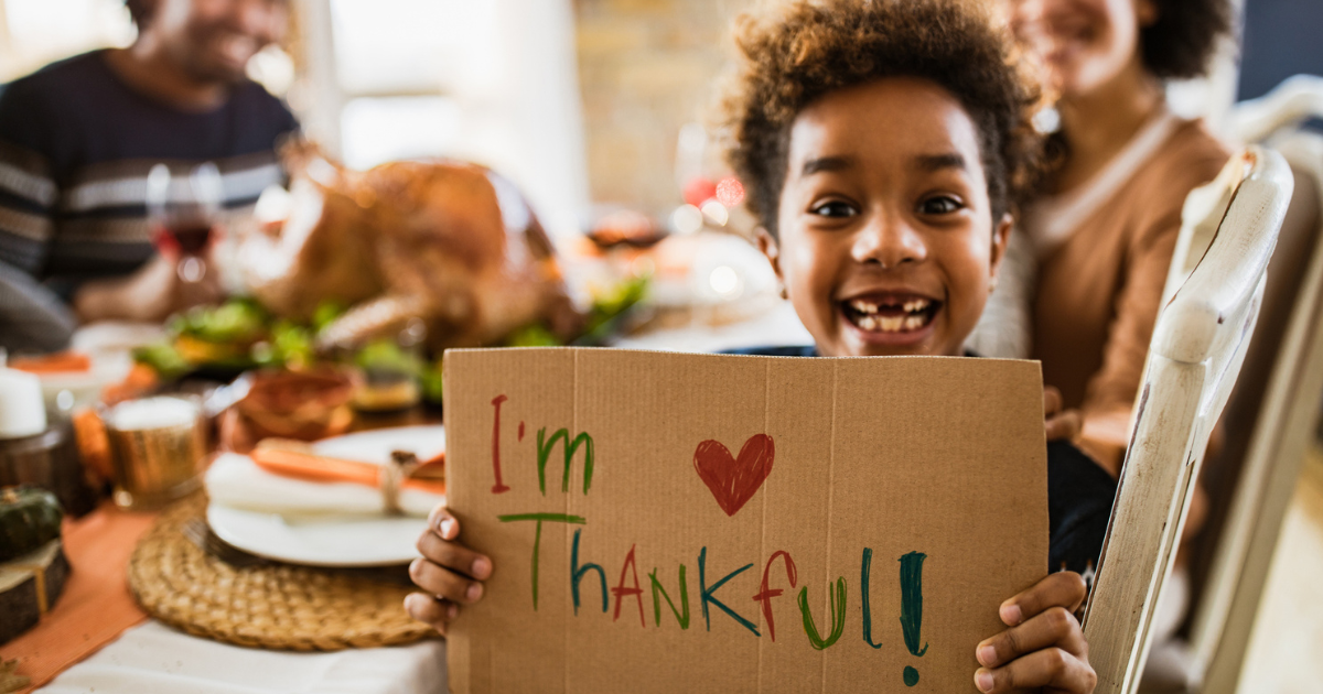 Young boy holding cardboard sign saying 'I'm thankful" at Thanksgiving dinner table