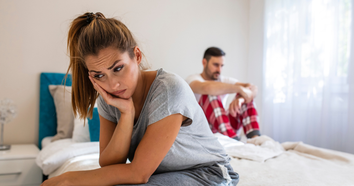 Woman and man sitting apart on bed