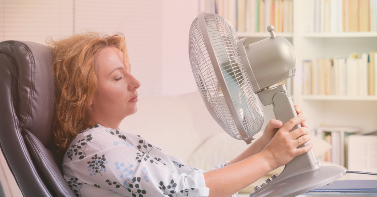 Woman sitting in an office chair and holding a desk fan to her face
