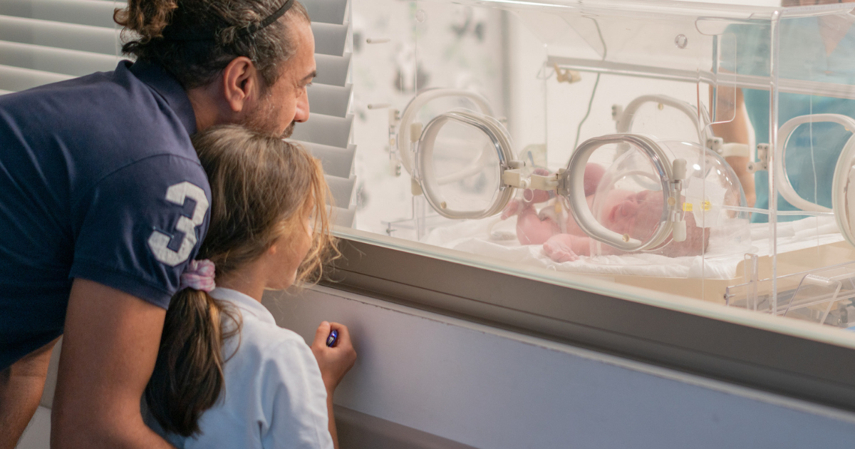 Dad and daughter look at baby sibling in incubator
