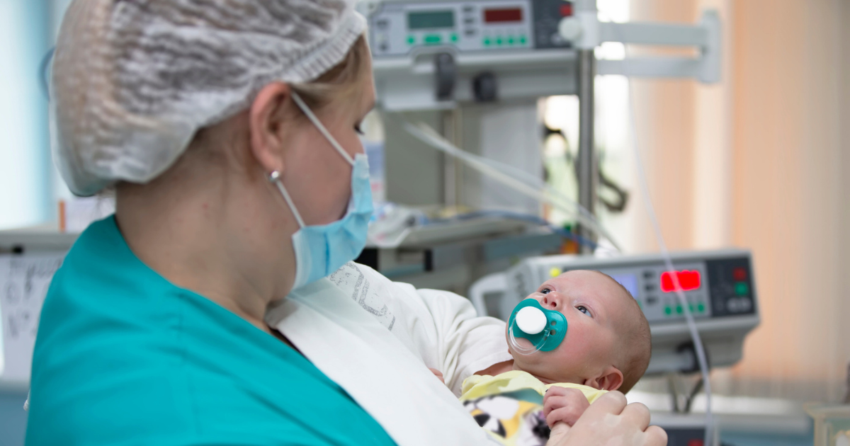 Woman in scrubs holding baby in NICU