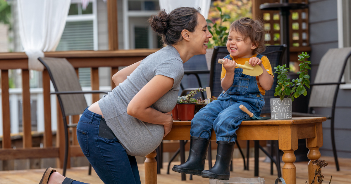 Pregnant woman laughing with her young daughter outside