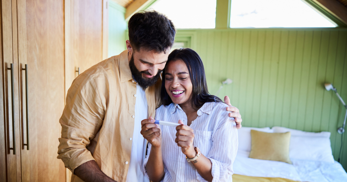 Man with his arm around woman holding pregnancy test