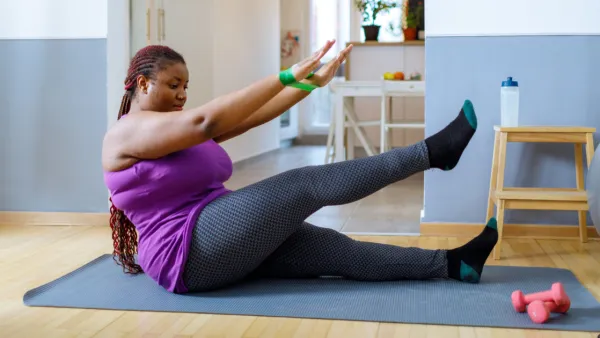 Woman sitting on exercise mat lifting leg and hand weight