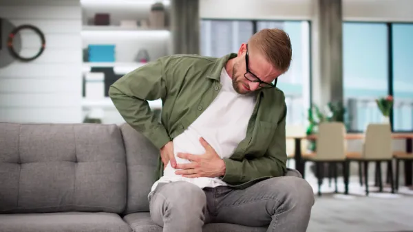 Man sitting on couch, holding abdomen in pain
