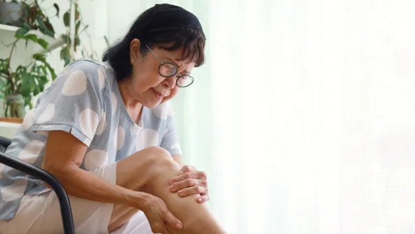 Older woman sitting, holding her leg in pain