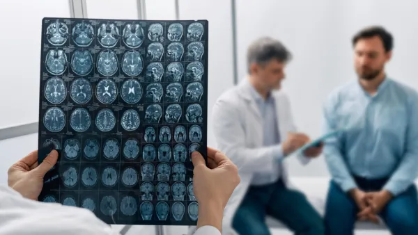 Doctor holding brain scans, doctor in background talking to man