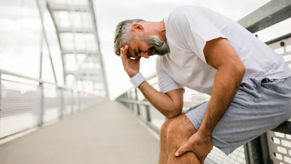 Man leaning against fence, holding his calf in pain