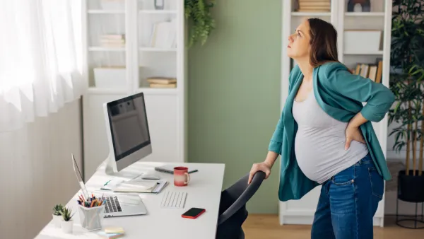 Pregnant woman standing in office holding her back