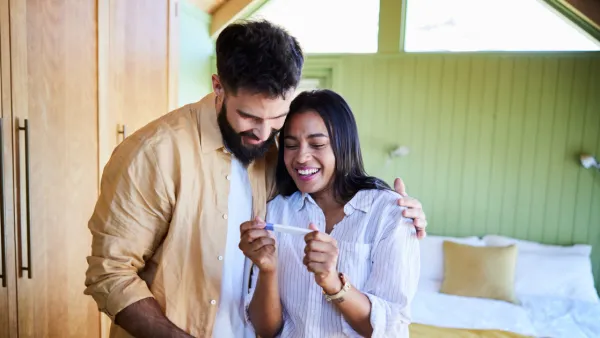 Man with his arm around woman holding pregnancy test