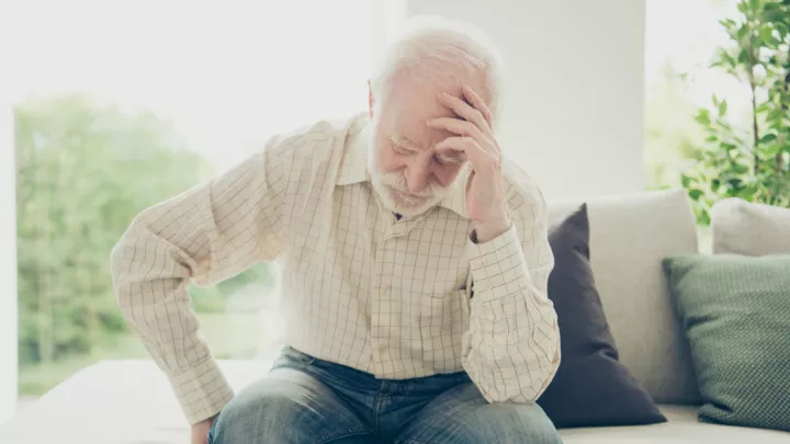 Older man sitting on the couch holding his head