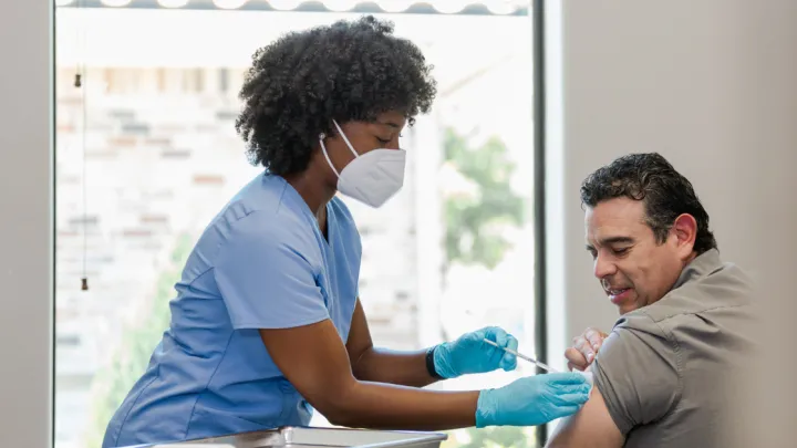 Nurse in protective mask and gloves gives man vaccination