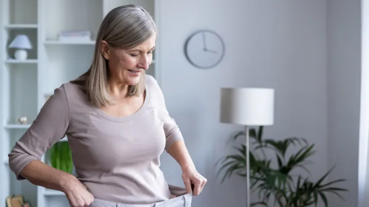 Older woman holding waistband of pants too large for her