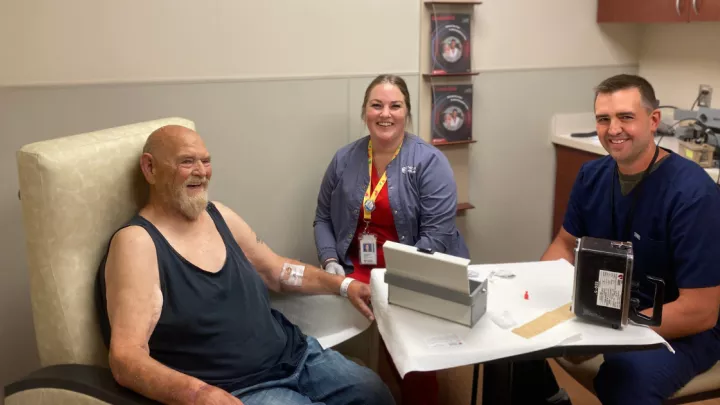 Craig Johnson, MD, Nuclear Medicine (right), and Beth McCaw, lead nuclear medicine technologist (center), administer the initial PLUVICTO dose to Phil Painter (left). 