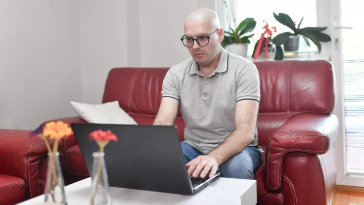 Male cancer patient sitting on the couch looking at laptop