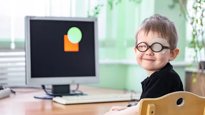 Young boy with patch over left eye and glasses sitting at computer