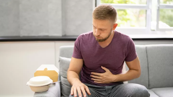 Man sitting on the couch holding his bloated stomach