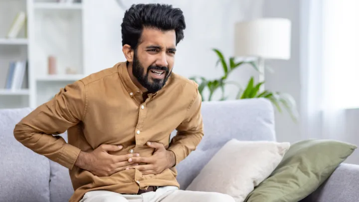 Man sitting on couch, holding abdomen in pain