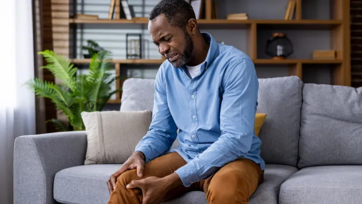 Man sitting on couch, holding leg in pain