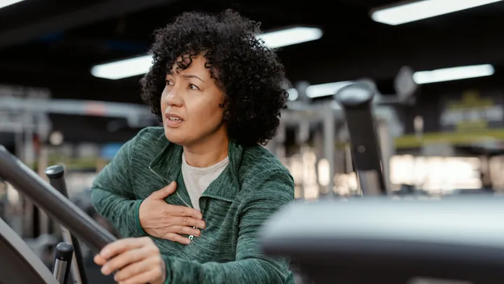 Woman on exercise machine holding chest in pain