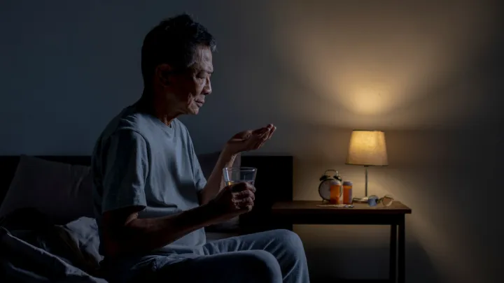 Older man sitting up in bed taking a pill