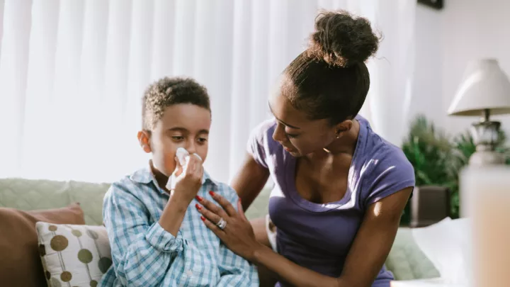 Child sitting on the couch with his mother, blowing his nose
