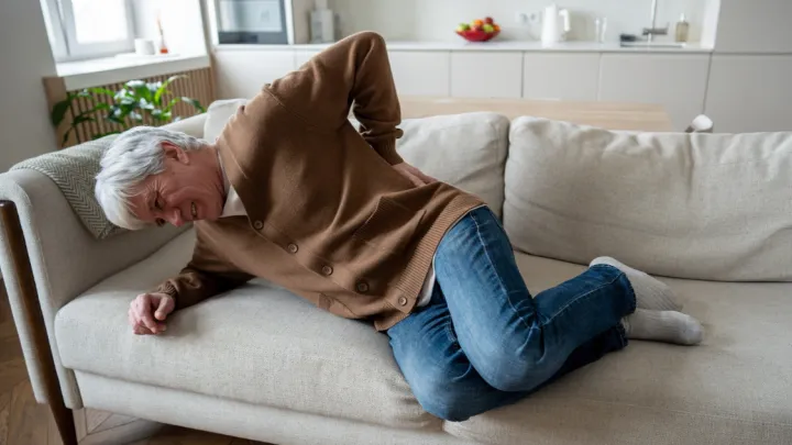 Man holding his back in pain lying on couch