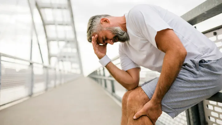 Man leaning against fence, holding his calf in pain