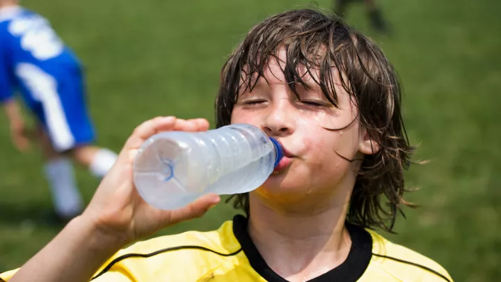 Young boy in a soccer uniform drinking water