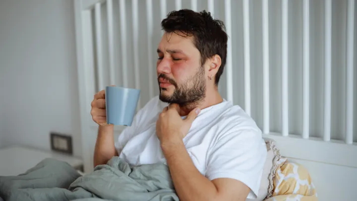 Sick man sitting in bed holding a mug