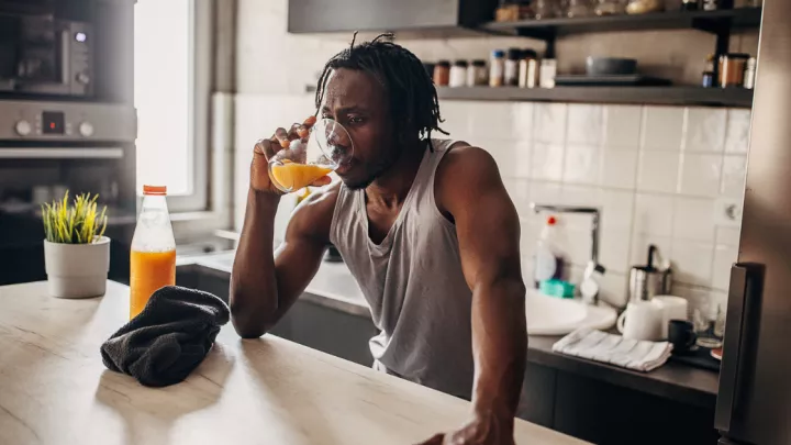 Man drinking a glass of orange juice in his kitchen