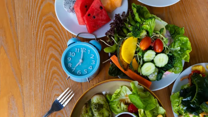 Alarm clock on table surrounded by plates of food.
