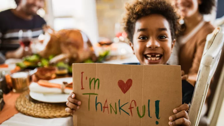 Young boy holding cardboard sign saying 'I'm thankful" at Thanksgiving dinner table