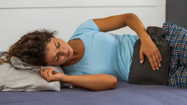 Woman lying in bed with hot water bottle on stomach
