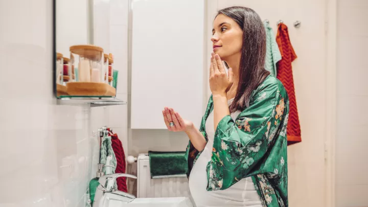 Pregnant woman applying a skin care product in her bathroom