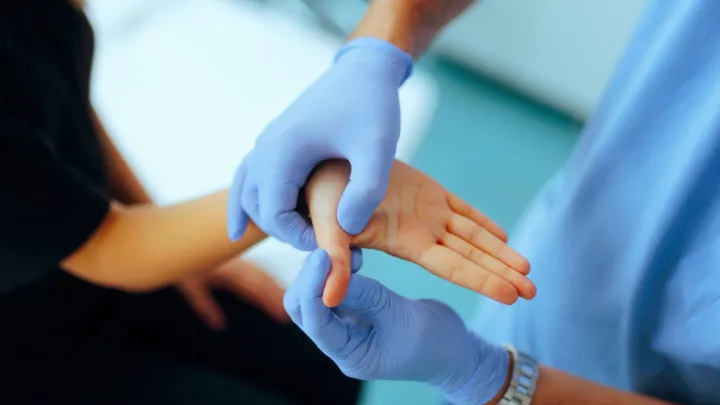 Close up of gloved hands inspecting patient's thumb