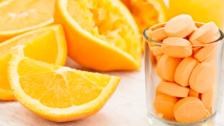 Quartered orange slices next to a cup full of vitamin C tablets