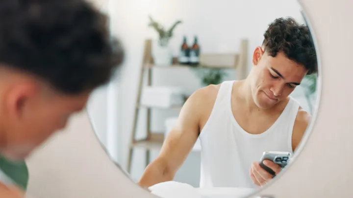Young man in mirror holding smartphone.