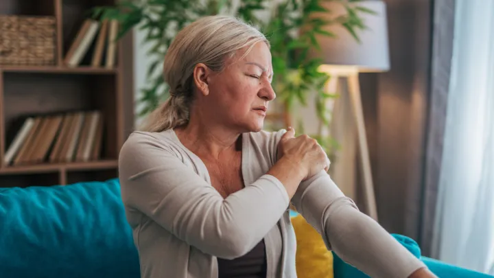 Woman sitting on couch holding arm in pain