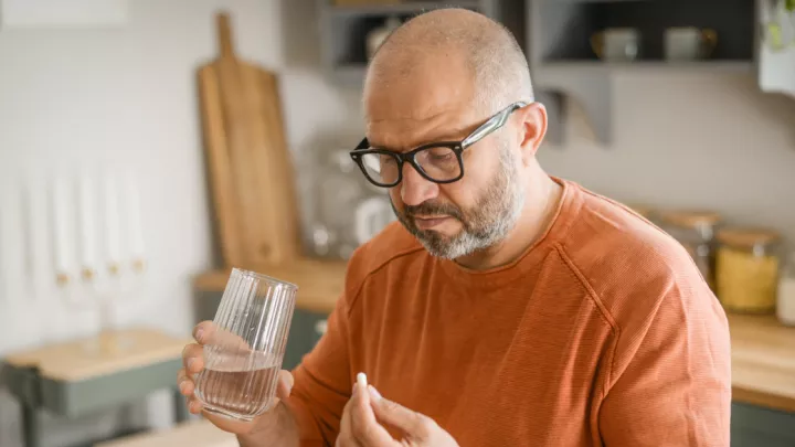 Man holding a pill and a glass of water
