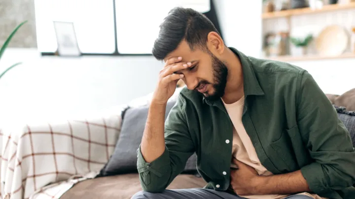 Man sitting on couch, holding stomach